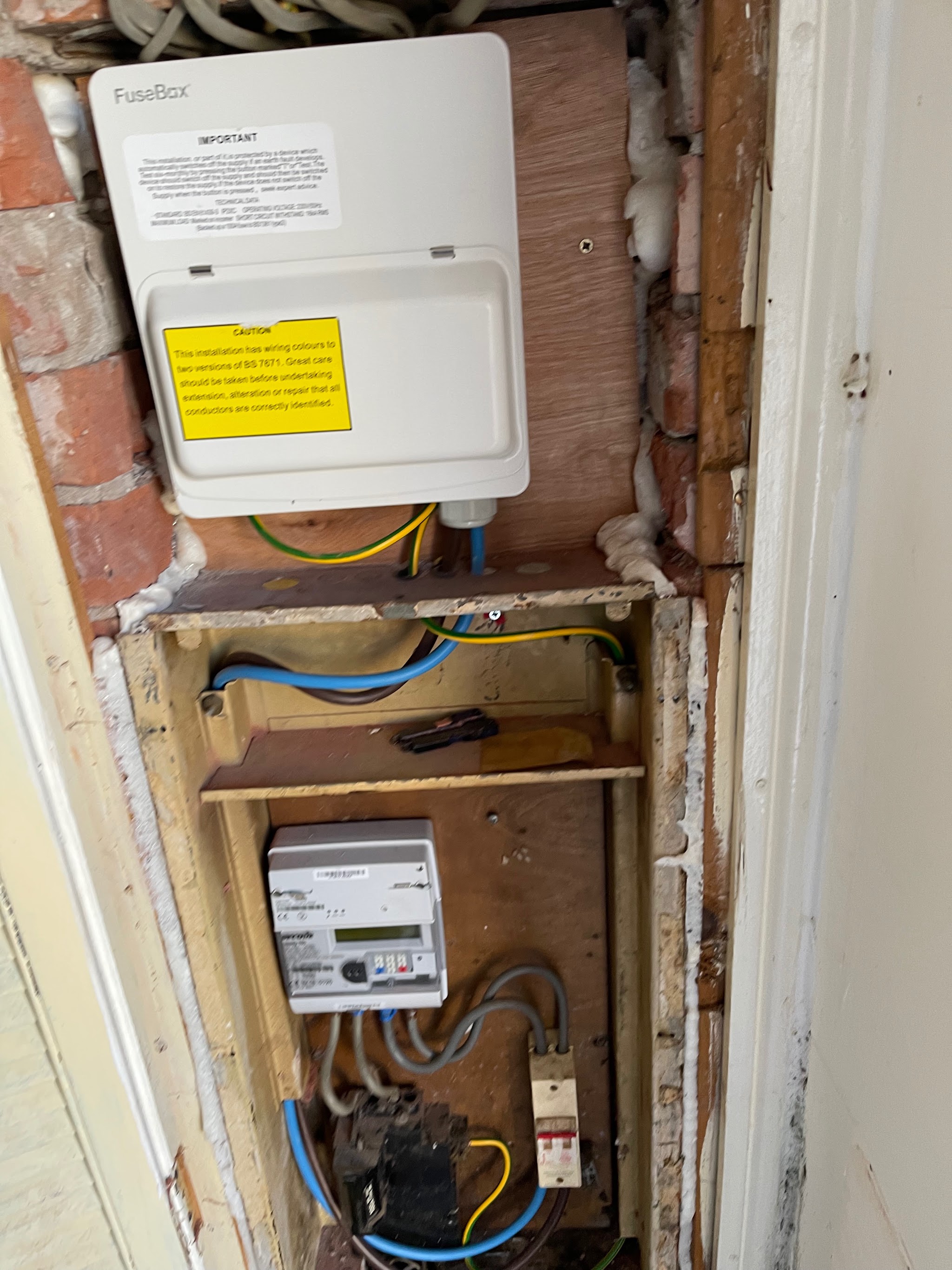 A consumer unit mounted above an opened-up meter recess in a brick wall