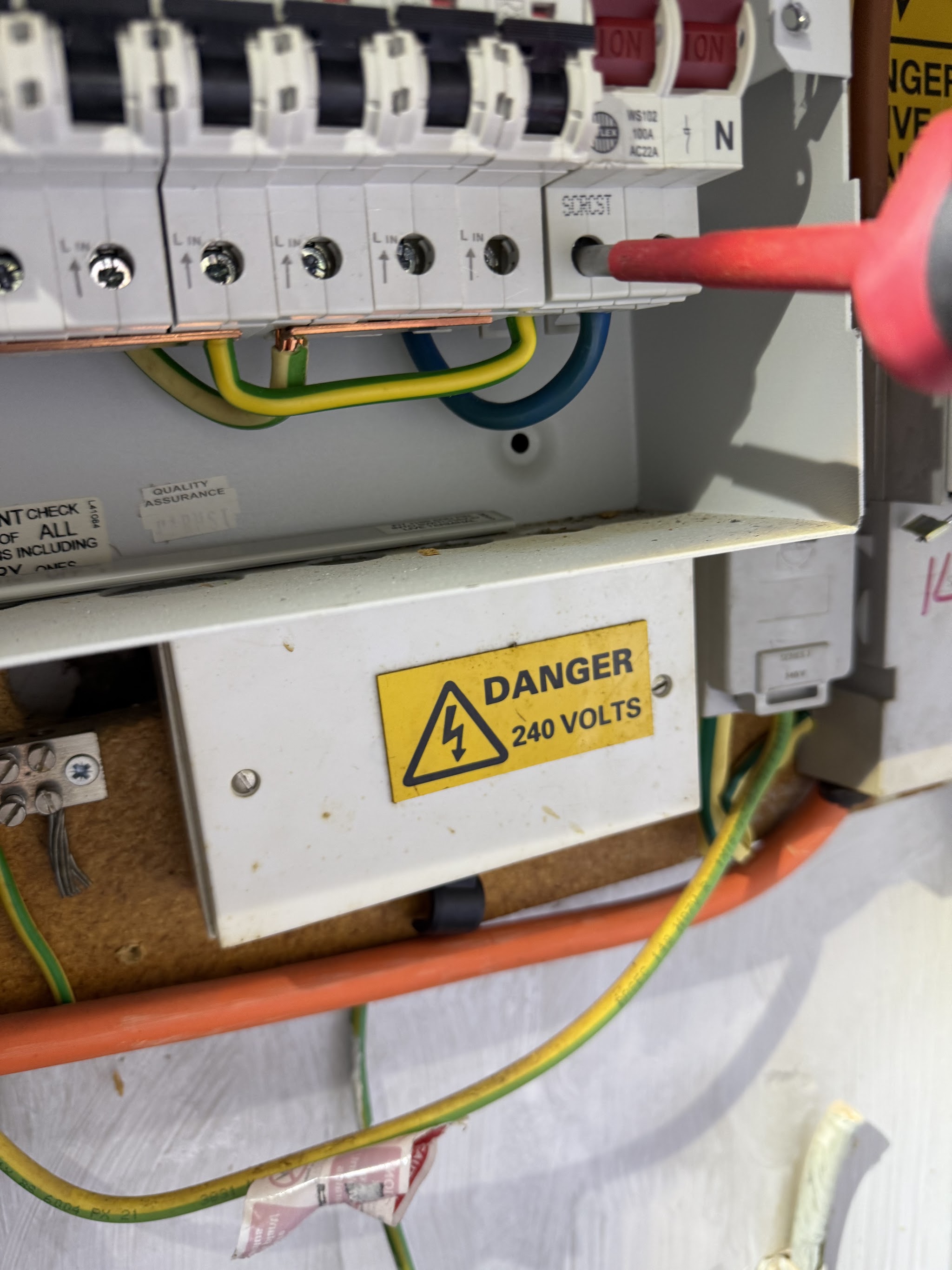An open consumer unit with an insulated screwdriver on the terminals and a danger label below